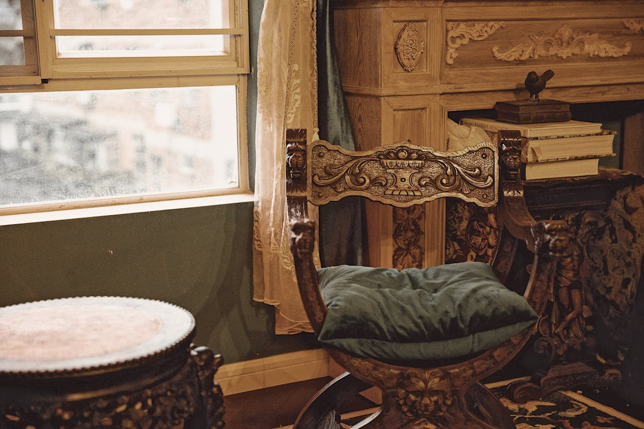 Luxury vintage interior featuring an ornate wooden chair beside a window with books and decor.