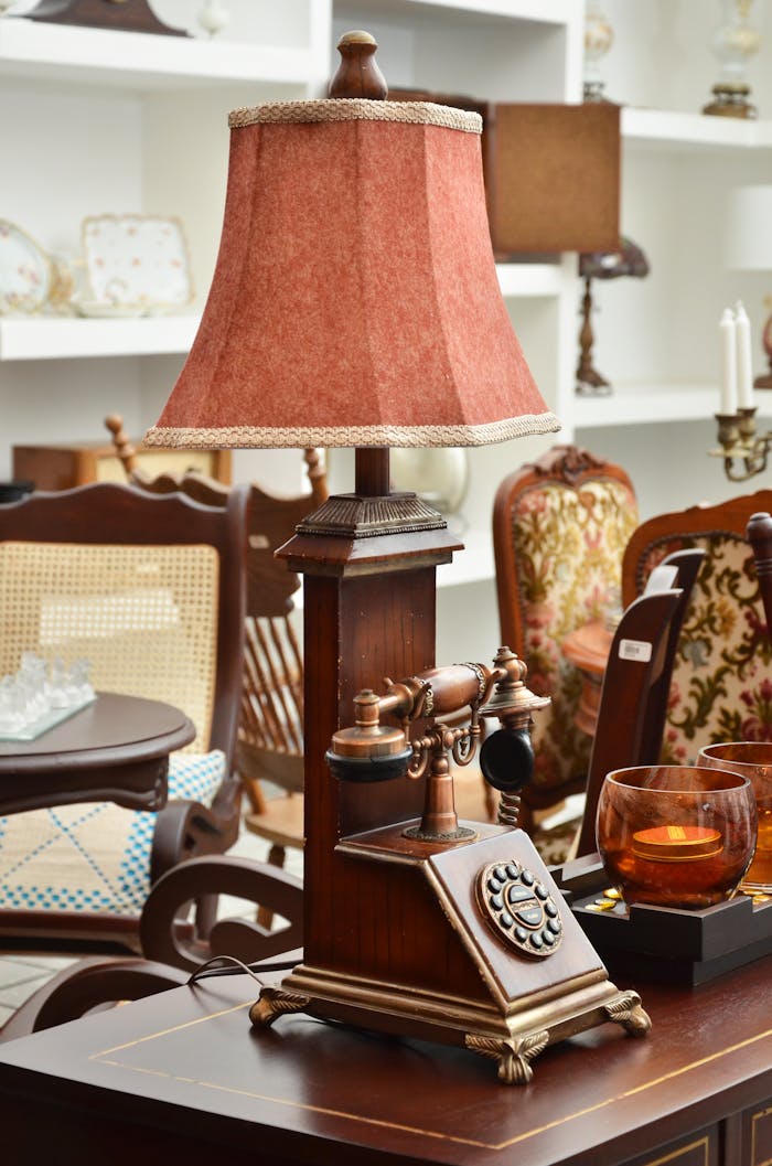 A vintage lamp and rotary telephone on a wooden table in a vintage furniture shop.